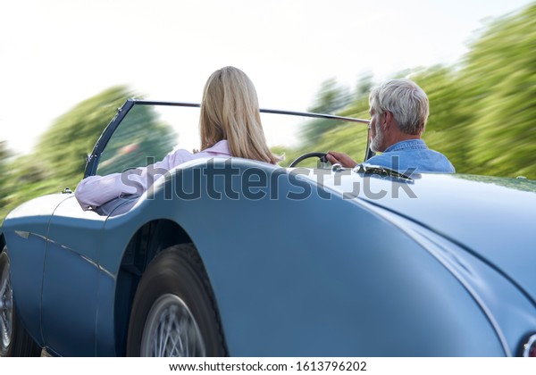 Rear View Of Mature Couple Enjoying Road\
Trip In Classic Open Top Sports Car Together\

