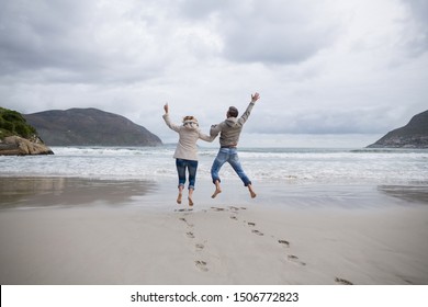 Rear view of mature couple jumping in air on the beach - Powered by Shutterstock