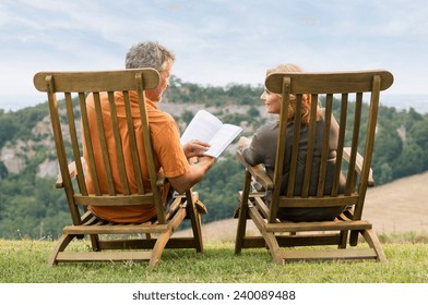 Rear View Of Mature Couple Sitting On Lounge Chair Reading Book - Powered by Shutterstock