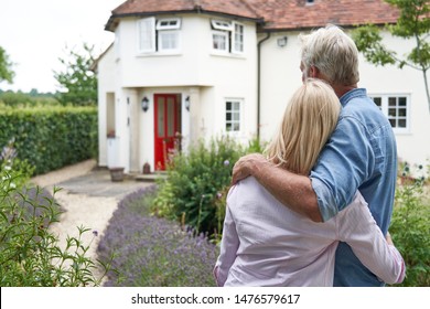 Rear View Of Mature Couple Standing In Garden Look At Dream Home In Countryside