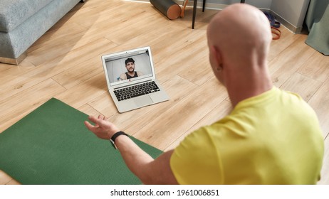 Rear View Of A Mature Male Fitness Instructor Explaining Workout Techniques Online While Having Video Conference, Conducting Virtual Fitness Class By Webcam On Laptop. Sport And Healthy Lifestyle