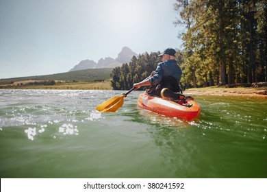 Rear View Of A Mature Man Canoeing In A Lake. Senior Man Paddling Kayak On A Summer Day.