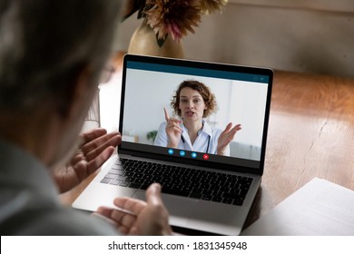 Rear View Of Mature Man Speak Talk On Video Call With Female Doctor, Have Online Consultation At Home. Elderly Male Patient Engaged In Webcam Digital Conversation On Computer With Nurse Or Caregiver.