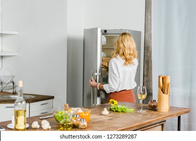 Rear View Of Mature Woman Taking Something From Fridge In Kitchen