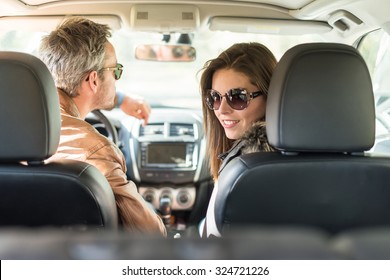 Rear View Of A Middle Aged Couple In A Black Seats Car. They Are About To Leave For The Weekend, Wearing Their Leather Coats And Sunglasses. The Smiling Woman Is Looking At Camera