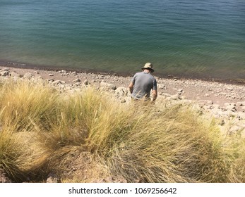 The rear view of a middle aged man walking down a grassy hill down to a rocky lake shore in front of blue water in Arizona
