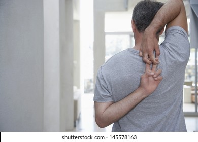 Rear View Of Middle Aged Man Stretching Arms Behind Back At Home