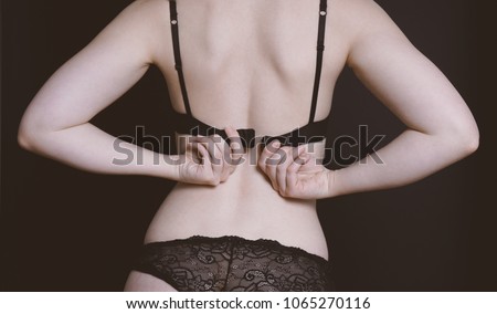 rear view of midsection of unrecognizable young woman undressing, opening her bra, taking off underwear