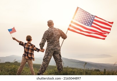 Rear View Of Military Man Father Holding   Son's Hand   With American Flag   And Enjoying Amazing Summer Nature View On Sunny Day, Happy Male Soldier Dad Reunited With Son After US Army