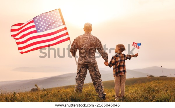 Rear\
view of military man father holding   son\'s hand   with american\
flag   and enjoying amazing summer nature view on sunny day, happy\
male soldier dad reunited with son after US\
army