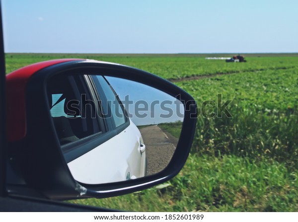 Rear\
view mirror of a car driving on a country road. Blurred view due to\
speed of the cultivated fields of southern\
Romania.