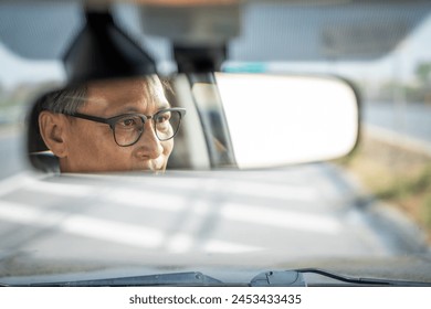 Rear view mirror. Close up shot eye of senior asian man looking roadway while driving car in the morning. Mature Man sitting in car. - Powered by Shutterstock