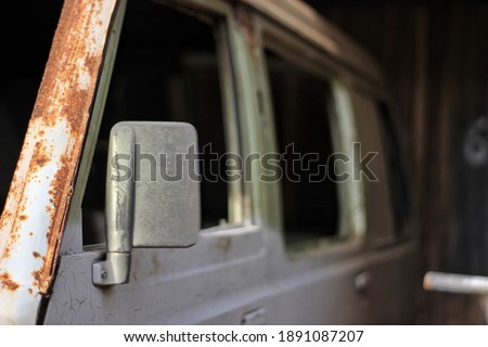 rear view mirror and rusty old car body visible from the side