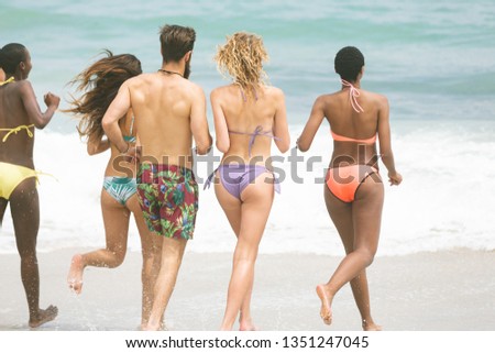 Rear view of multi ethnic group of friends running at beach on sunny day