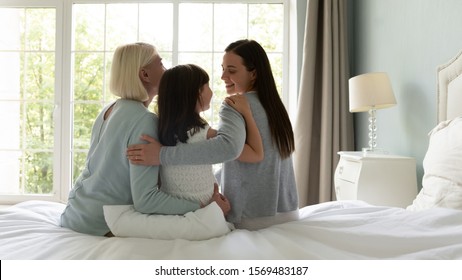 Rear View Multi Generational Family Diverse Generations Of Women Enjoy Heart-to-heart Talk Sit On Bed In Cozy Bedroom, Elderly Grandma Grown Up Daughter Granddaughter Threesome Spend Good Time At Home