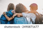 Rear view of multiethnic elementary middle school kids pupils classmates friends with backpack in casual clothes are hugging embracing each other standing outdoors.