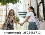 Rear view of multiethnic elementary middle school girls gen Alpha pupils classmates with backpack in casual clothes are hugging embracing each other standing outdoors. Part of a series.