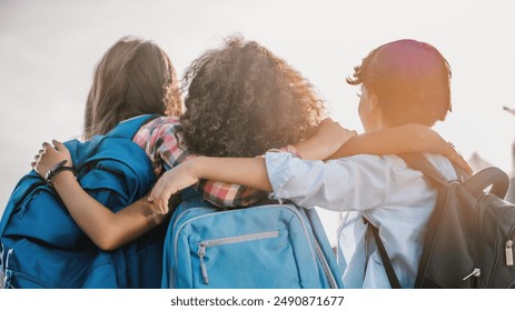 Rear view of multiethnic elementary middle school kids pupils classmates friends with backpack in casual clothes are hugging embracing each other standing outdoors.