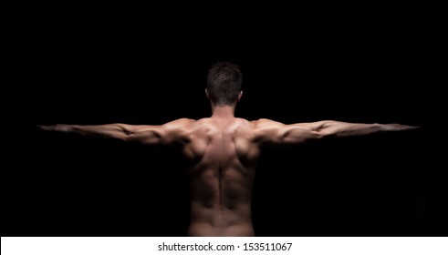 Rear View Of A Muscular Man With Arms Stretched Out On Black Background