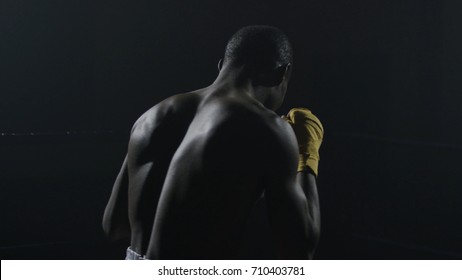 Rear view of muscular man boxing on black background. Afro american young male boxer practicing shadow boxing. Boxer in yellow Boxing gloves - Powered by Shutterstock