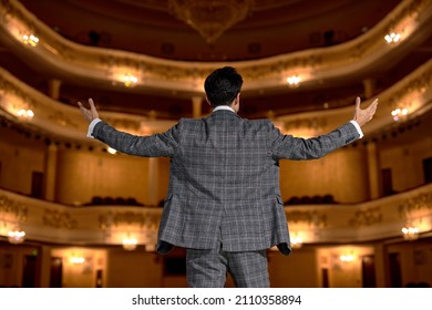 Rear View On Caucasian Brunette Man In Elegant Stylish Gray Suit Performing Opera Or Singing At A Concert Or Show, Talented Guy In Give Performance To Audience People On Stage. Presentation Stage.