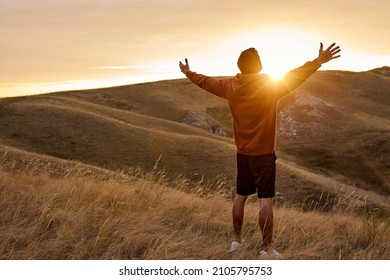 rear view on guy on top of mountain reaches for the sun during sunrise, feel happiness, enjoy the morning outdoors in nature on fresh air. in field. achievement, beginning, happiness, human emotions