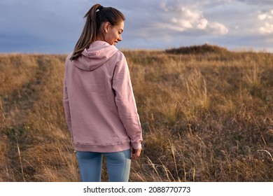 Rear view on happy female in pink hoodie and leggins standing in field in the morning. view from back on long-haired lady going to train on fresh air outdoors, at sunrise. people lifestyle concept - Powered by Shutterstock