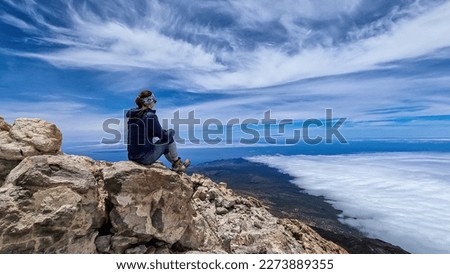 Rear view on hiking woman sitting on rock enjoying panorama from summit of volcano Pico del Teide on the island of Tenerife, Canary Islands, Spain, Europe. Island covered in cloud. Freedom concept