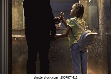 Rear view on unrecognizable man with child standing in lift, elevator, view from back. man give candy. little girl is very gullible, don't afraid of adult man, holding hands together