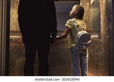 Rear View On Unrecognizable Man With Child Standing In Lift, Kidnapping Children Concept. Copy Space. View From Back. Little Girl Is Very Gullible, Don't Afraid Of Adult Man, Holding Hands Together