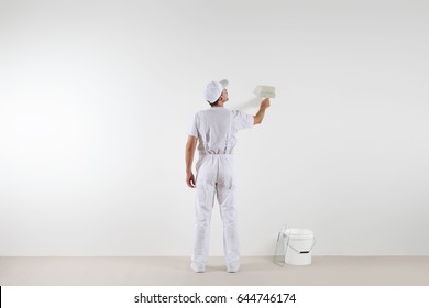 Rear view of painter man looking at blank wall, with paint brush and bucket, isolated on white room