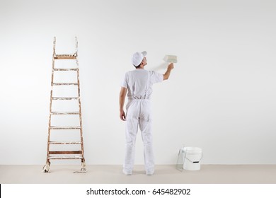 Rear view of painter man looking and painting blank wall, with paint brush, bucket and wooden ladder, isolated on white big space