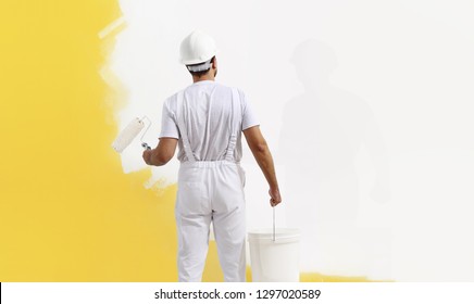 Rear view of painter man painting the wall, with paint roller and bucket, isolated on big empty copy space template