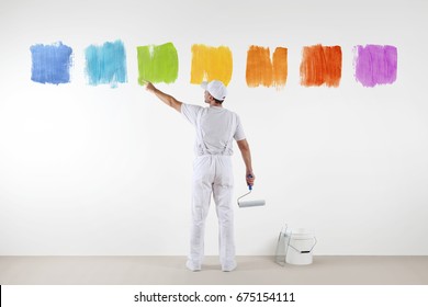 Rear View Of Painter Man Pointing With Finger The Colors On Wall, With Paint Roller And Bucket, Isolated On White