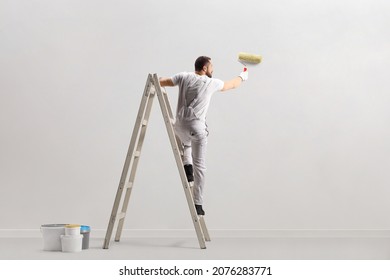 Rear view of a painter painting a wall on a ladder isolated on white background - Shutterstock ID 2076283771