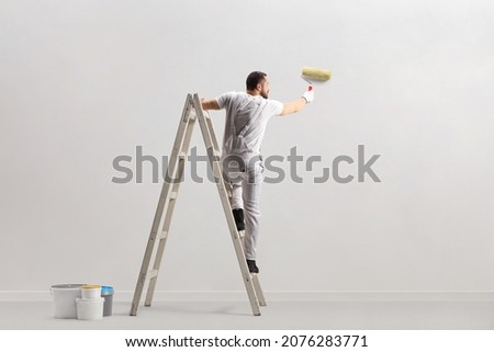 Rear view of a painter painting a wall on a ladder isolated on white background