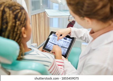 Rear View Of Patient And Doctor Examining The X-ray Image On Digital Tablet At Dental Clinic