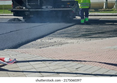 rear view of a paver, road paving machinery, being operated by workers to apply new asphalt that will be used to renovate a street. Bitumen and tar used to renew the pavement at roadwork. - Shutterstock ID 2175060397