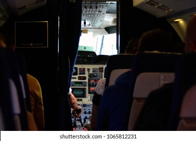 Rear View Of People Sitting And Waiting Airplane To Take Off, Cockpit Door Is Open, Still At The Airport