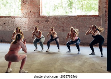 Rear View Of A Personal Trainer Giving Gymnastics Class To A Group Of Women With Different Body Shapes - Jumping Squat Hit Workout