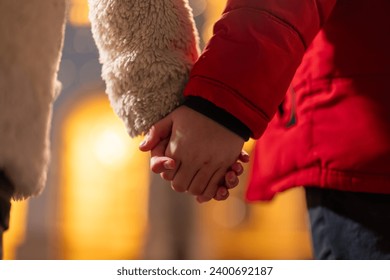 Rear view photo of boy and girl holding hands while walking. Focus is on the hands. Unrecognizable young children walking hand in hand in the evening on the city street. - Powered by Shutterstock