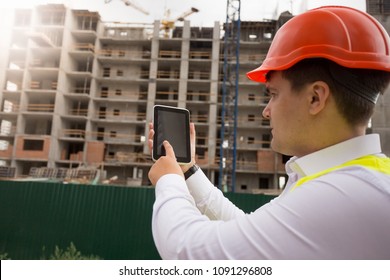 Rear view photo of male building worker using digital tablet on construction site