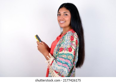 Rear View Photo Portrait Of Young Hispanic Woman Wearing Colourful Clothes Over White Background Using Smartphone Smiling