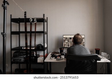 Rear view of a photographer reviewing photographs on a computer in a well-organized home studio with camera equipment. - Powered by Shutterstock