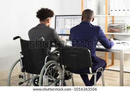 Rear View Of Physically Impaired Businessman With His Partner Working On Computer On Desk