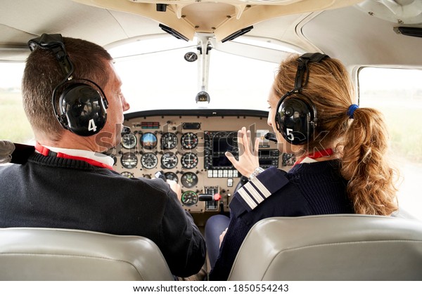 Rear view of pilot trainee and female\
flight instructor in cockpit. He is sitting next to the female\
instructor attending to her\
explanations.