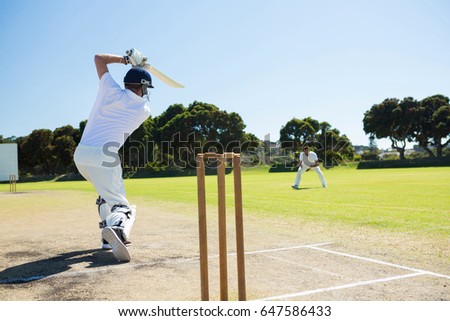 Rear view of player batting while playing cricket on field against clear sky