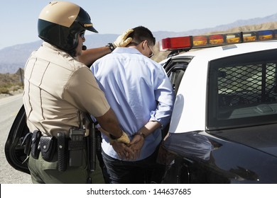 Rear view of a police officer guiding apprehended man into police car