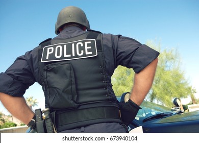 Rear View Of Policeman In Uniform Standing Against Car