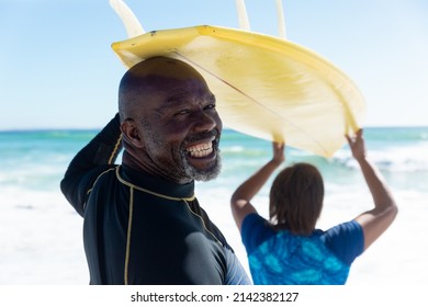 Rear view portrait of african american senior man carrying surfboard on head with woman at beach. unaltered, togetherness, active lifestyle, aquatic sport and holiday concept. - Powered by Shutterstock